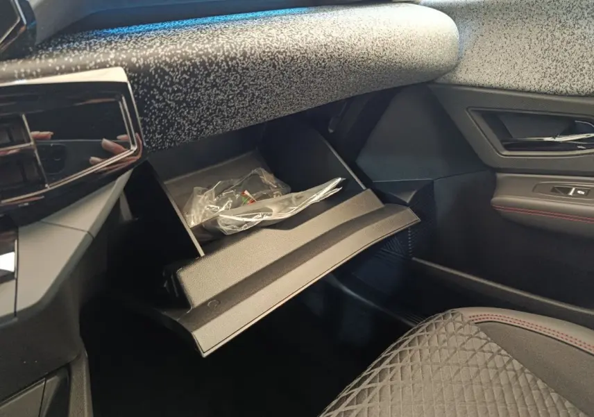 Intérieur de la Renault Clio Techno 2026, vue côté passager avec boîte à gants ouverte et sellerie noire à surpiqûres rouges.