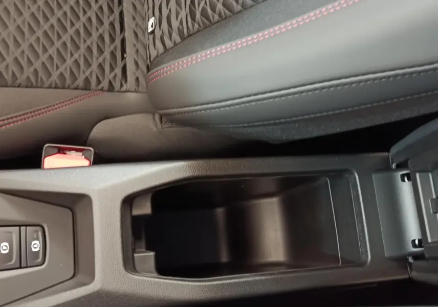 Gros plan sur l'accoudoir central avant ouvert de la Renault Clio Techno gris foncé avec surpiqûres rouges et sellerie tissu.