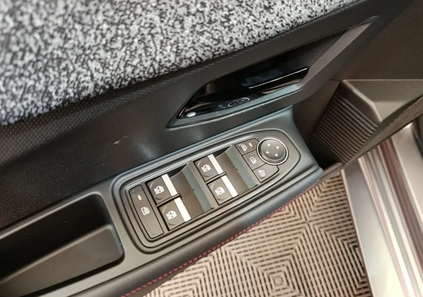 Gros plan sur la commande des vitres électriques côté conducteur d'une Renault Clio gris foncé, avec surpiqûres rouges.