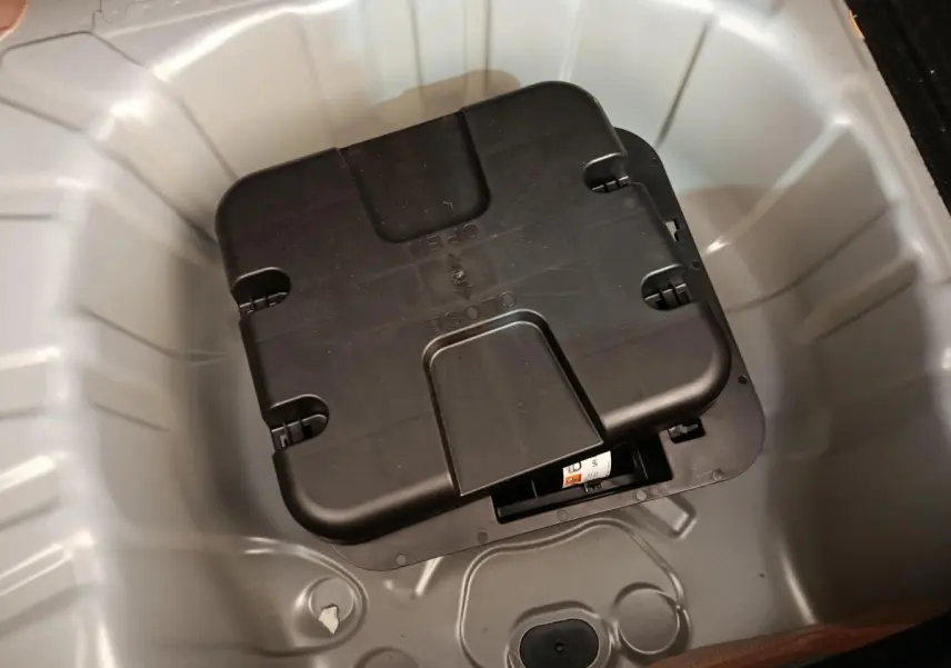 Coffre ouvert en vue plongeante montrant le rangement gris clair sous la tablette avec un boîtier noir au centre.