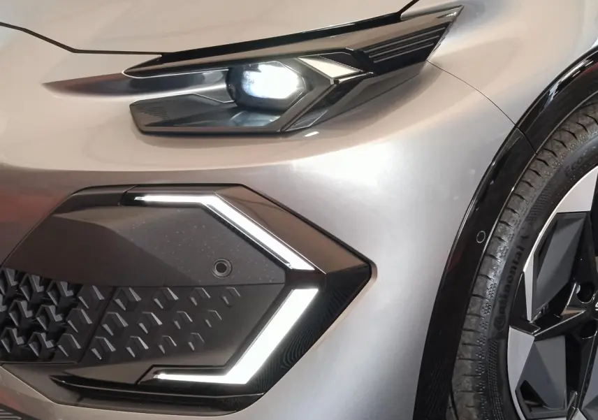 Gros plan sur l'avant droit de la Renault Clio Techno gris foncé, mettant en valeur le phare LED et la calandre géométrique.