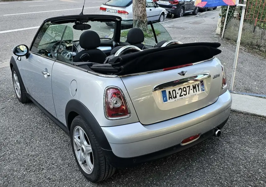 Vue 3/4 arrière d'une MINI Cabriolet R57 grise de 2010 avec capote noire repliée et jantes argentées.