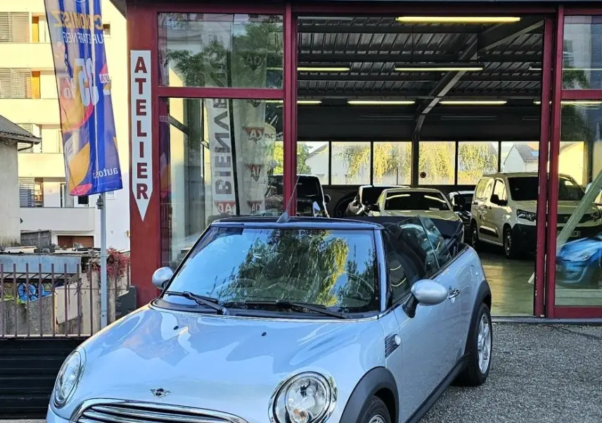 MINI Cabriolet R57 grise vue 3/4 avant droit, capote noire, stationnée devant un garage AD Expert.