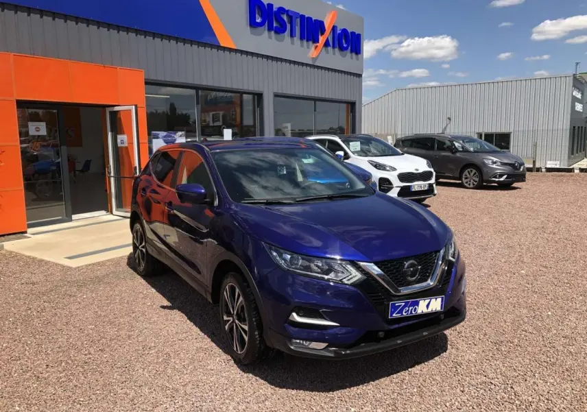 Nissan Qashqai bleu métallisé en 3/4 avant droit, stationné devant un concessionnaire avec panneau Distinxion visible.