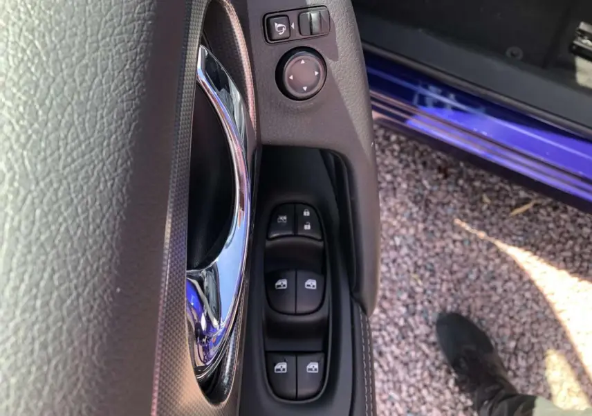 Gros plan sur la commande des vitres électriques côté conducteur du Nissan Qashqai bleu, avec poignée chromée visible.