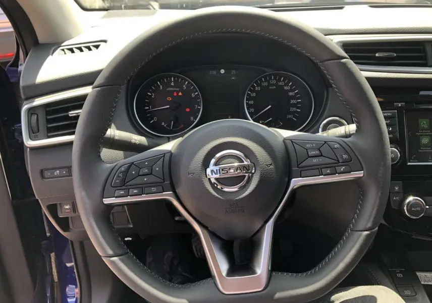Vue centrée sur le volant cuir du Nissan Qashqai bleu, avec commandes intégrées et tableau de bord visible.