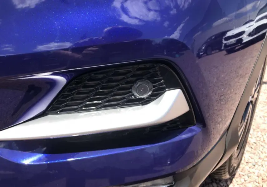 Gros plan sur la calandre avant droite du Nissan Qashqai 2019 bleu Topaze avec caméra de vision 360° intégrée.