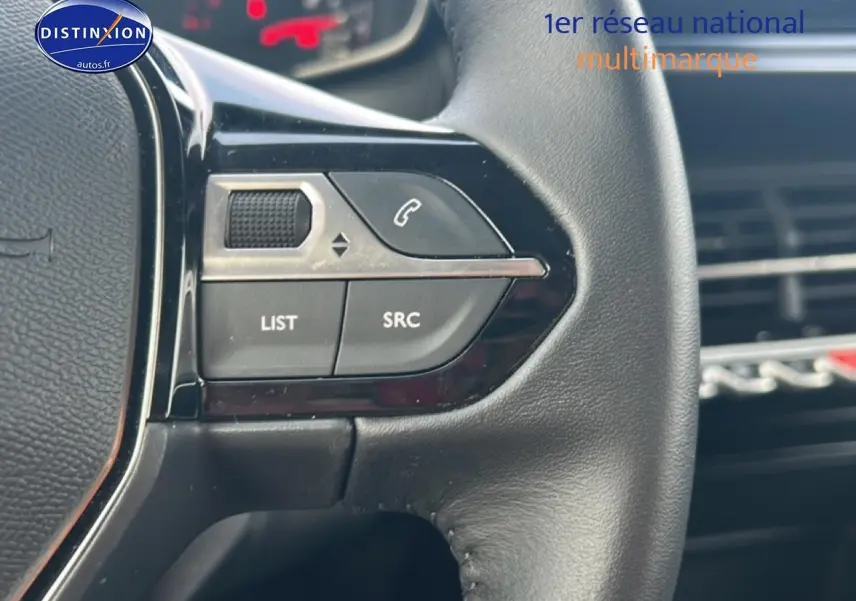 Gros plan sur les commandes audio au volant noir du Peugeot 208 1.2 100 style, intérieur moderne avec tableau de bord flou.