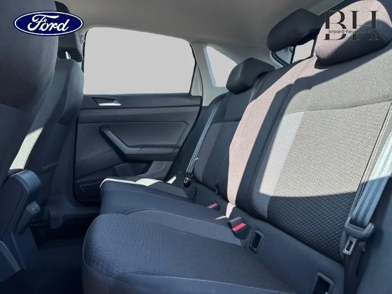 Vue latérale intérieure des sièges arrière en tissu noir du Volkswagen Taigo 2024, avec ceintures de sécurité visibles.