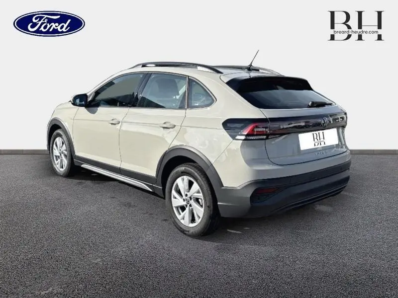 Vue 3/4 arrière droite d'un Volkswagen Taigo blanc pur avec barres de toit et jantes alu sur fond neutre.