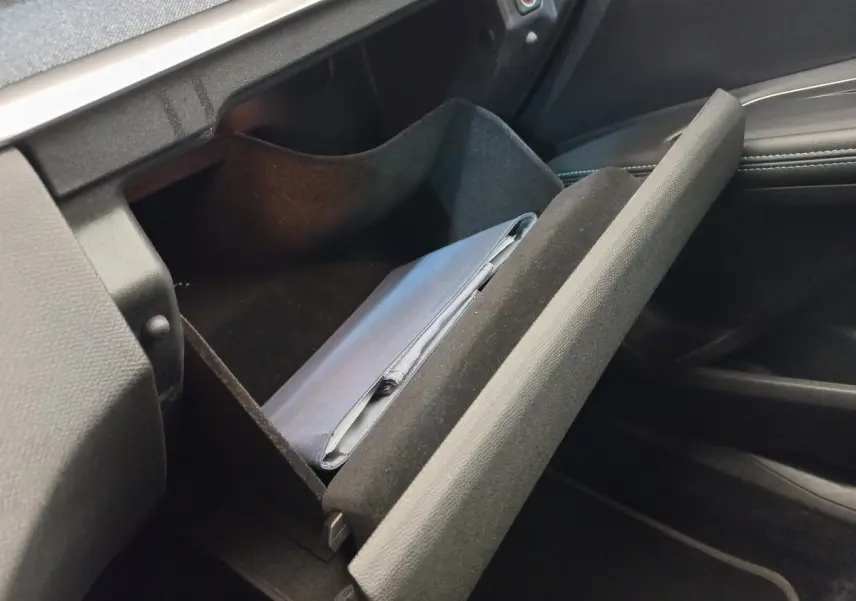 Gros plan sur la boîte à gants ouverte côté passager du Peugeot 5008 gris foncé, avec un manuel à l'intérieur.