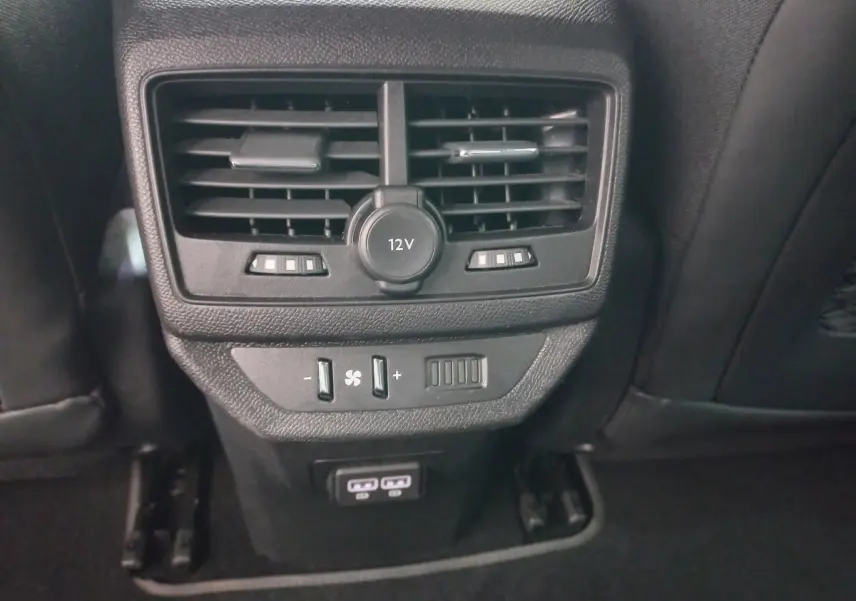 Gros plan sur la console arrière noire du Peugeot 5008 avec bouches d’aération, prise 12V et commandes de ventilation.