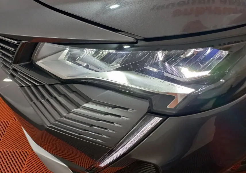 Gros plan sur le phare avant droit LED et la calandre d’une Peugeot 5008 gris foncé, finition Allure Pack.