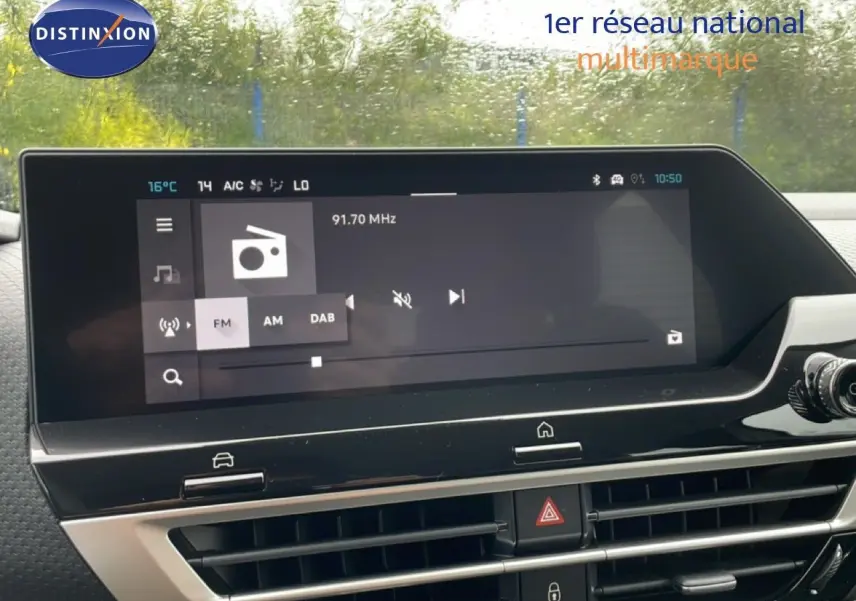 Écran tactile central de la Citroën C4 PureTech blanc métal affichant la radio FM, avec commandes et aérateurs en vue frontale.