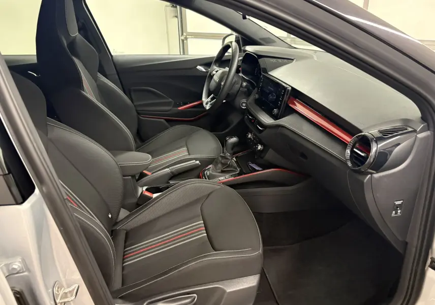 Vue intérieure côté conducteur de la Skoda Fabia 2025 gris argent, avec sièges sport noirs et inserts rouges sur tableau de bord.