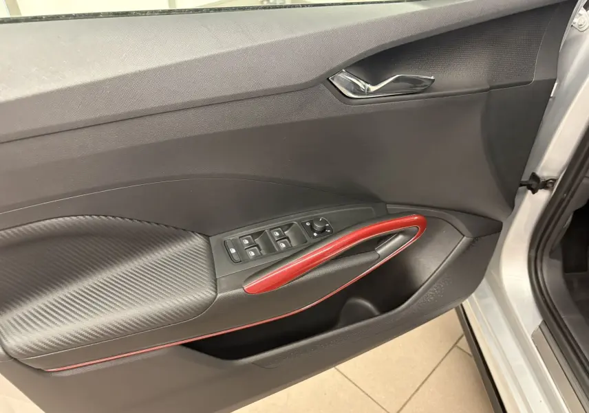 Vue intérieure côté gauche de la porte avant d'une Skoda Fabia 2025 gris argent avec poignée rouge et commandes électriques.