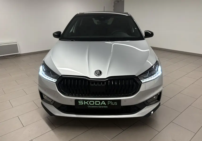 Vue frontale d'une Skoda Fabia 2025 gris argent avec toit noir, phares LED allumés dans un showroom.