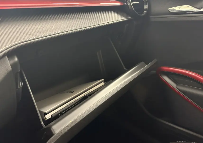 Gros plan sur la boîte à gants ouverte de la Skoda Fabia Monte Carlo 2025, avec garniture intérieure noire et détails rouges.