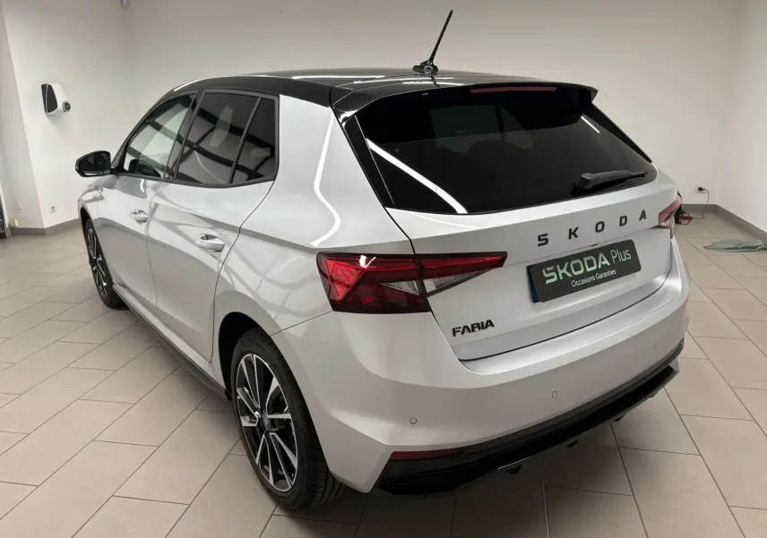 Vue 3/4 arrière droite d'une Skoda Fabia 2025 gris argent avec toit noir et jantes alliage noires en intérieur showroom.