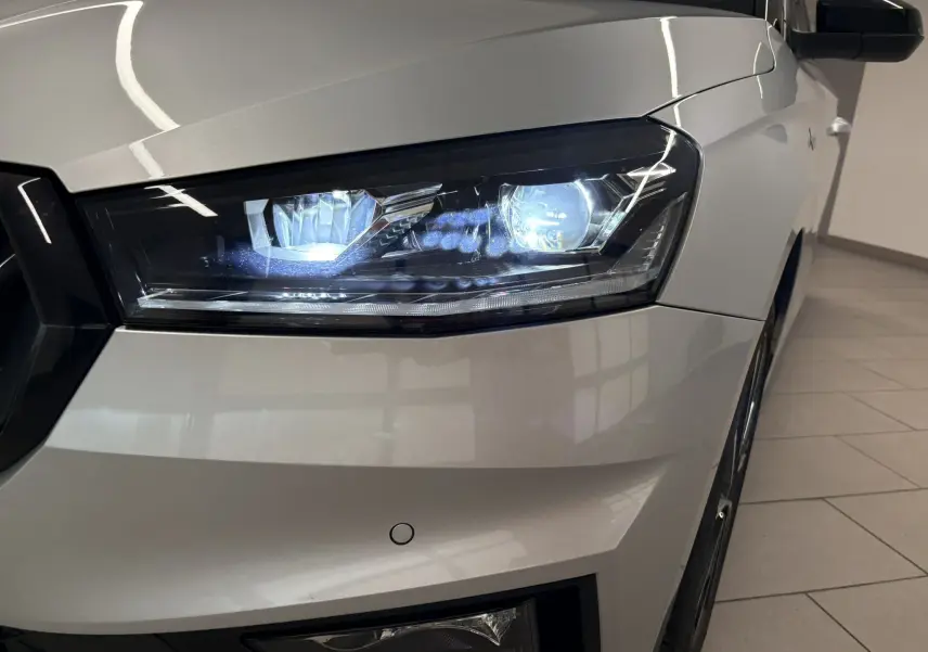 Gros plan sur le phare avant droit allumé d'une Skoda Fabia 2025 gris argent avec toit noir, vue de face côté droit.
