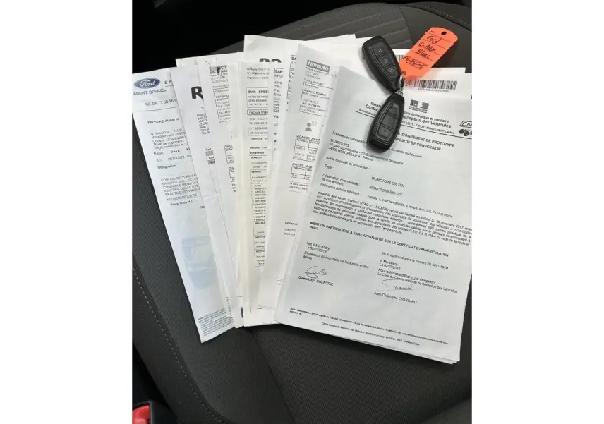 Clé de voiture Ford C-MAX blanche posée sur plusieurs documents sur un siège intérieur noir.