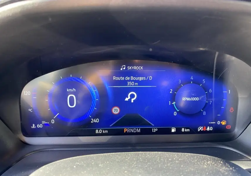 Vue rapprochée du tableau de bord numérique bleu du Ford Puma gris 2021, affichant vitesse, régime et navigation.