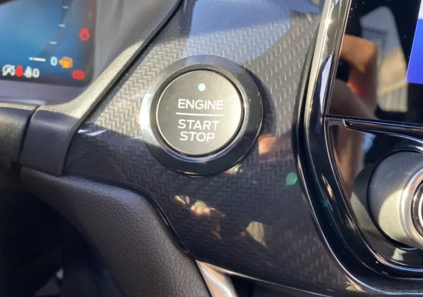 Gros plan sur le bouton Engine Start Stop entouré d’un décor noir à effet carbone dans le tableau de bord d’une Ford Puma gris 2021.