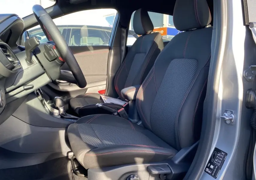 Vue intérieure côté conducteur du Ford Puma gris 2021, sièges tissu noir avec surpiqûres rouges et volant multifonctions.
