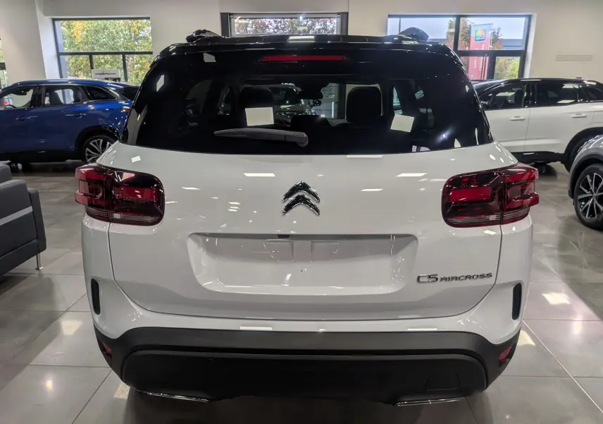 Vue arrière d'un Citroën C5 Aircross hybride blanc Okénite avec toit noir, en showroom lumineux.