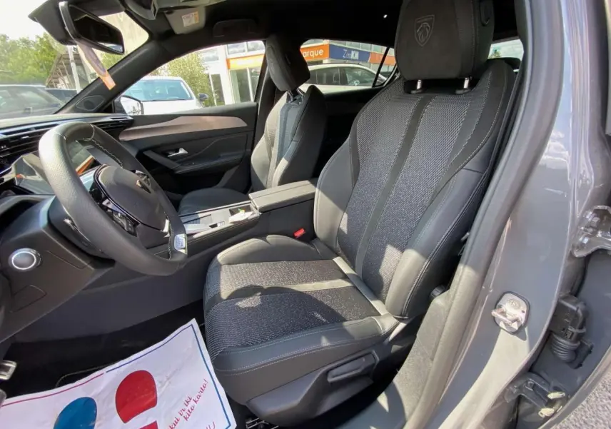 Intérieur avant droit de la Peugeot 308 GT 2025 gris selenium, sièges en tissu et cuir avec logo Peugeot brodé sur l'appui-tête.