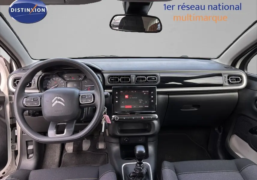 Vue intérieure avant du tableau de bord et volant d'une Citroën C3 blanc banquise 2022 avec boîte manuelle et écran tactile central.