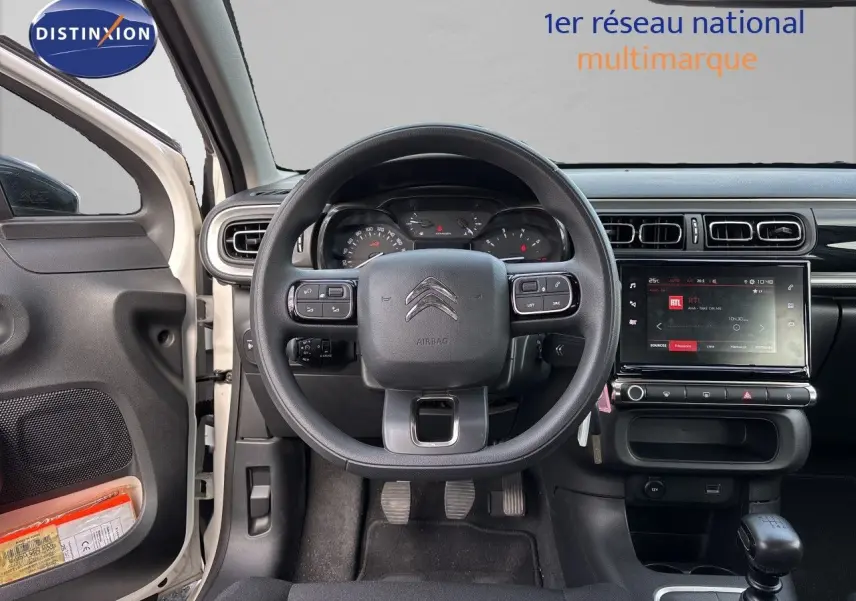 Vue intérieure centrée sur le volant et tableau de bord d'une Citroën C3 blanc banquise, avec écran tactile et portière ouverte côté gauche.