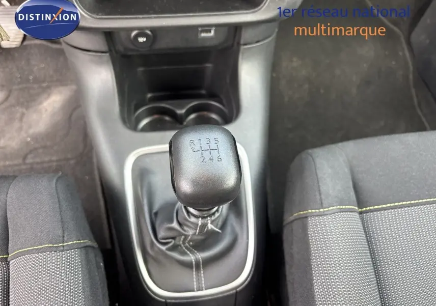 Vue rapprochée de la commande de boîte manuelle noire entourée de surpiqûres blanches dans l’habitacle du Citroën C3 blanc.