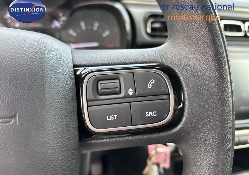 Gros plan sur les commandes gauche du volant noir de la Citroën C3 blanche, avec boutons de gestion audio et appel.