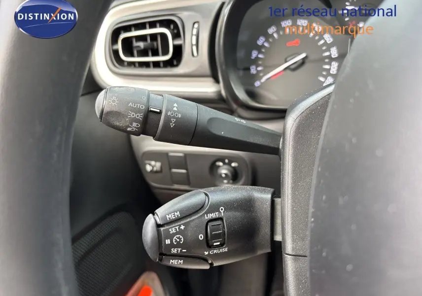 Gros plan sur les commandes au volant côté gauche de la Citroën C3 blanche, avec tableau de bord et aérateur visibles.