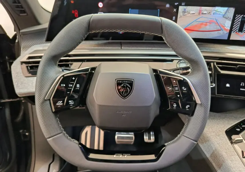 Vue rapprochée du volant cuir gris perforé Peugeot 3008 1.2 Hybrid GT avec commandes multifonctions et logo central.