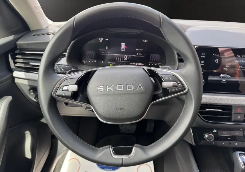 Vue intérieure centrée sur le volant SKODA gris foncé avec tableau de bord numérique et écran tactile central.
