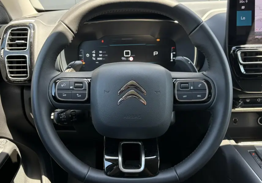 Vue frontale centrée sur le volant noir cuir du Citroën C5 Aircross Hybrid 2025 avec commandes intégrées et tableau de bord numérique.
