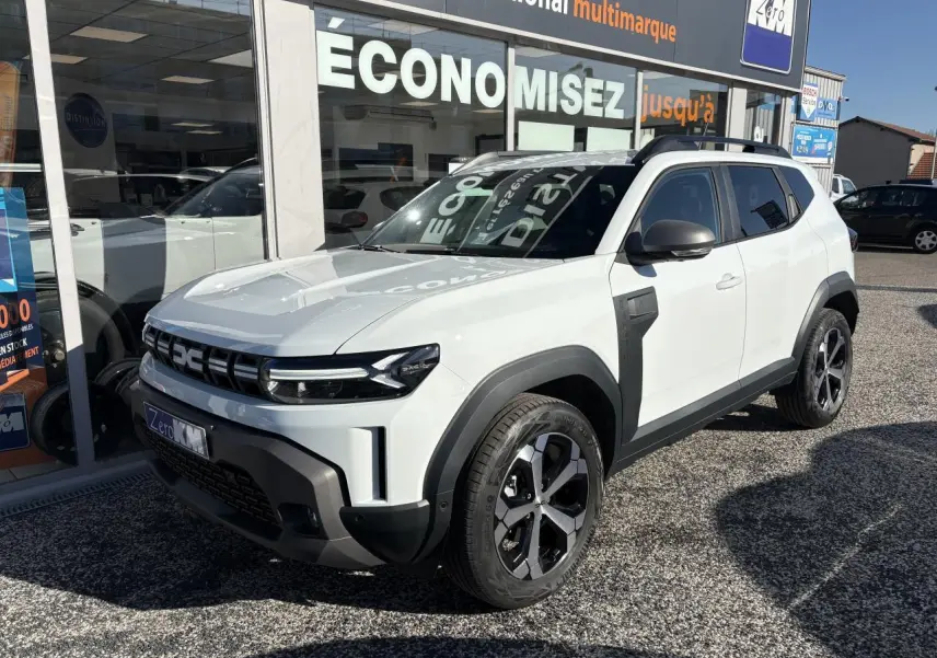 Dacia Duster blanc métallisé vu en 3/4 avant droit, avec barres de toit noires et jantes alliage distinctives.