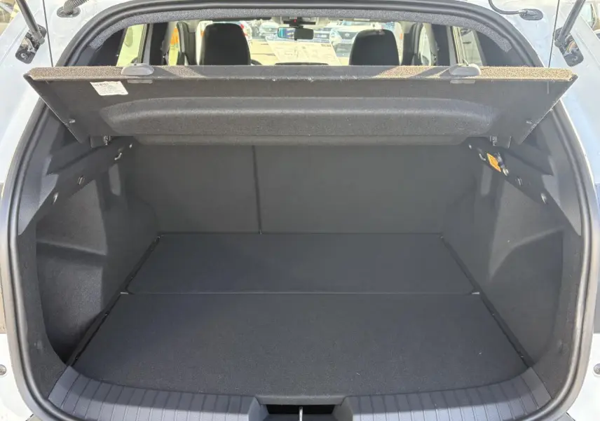 Coffre ouvert d'un Dacia Duster blanc métallisé 2024, vue arrière montrant l'espace de chargement vide et le cache-bagages relevé.