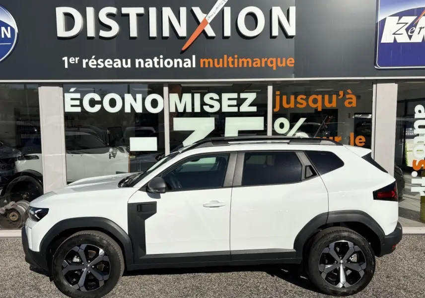 Profil côté gauche du Dacia Duster 2024 blanc métallisé avec barres de toit noires et jantes alliage 18 pouces.