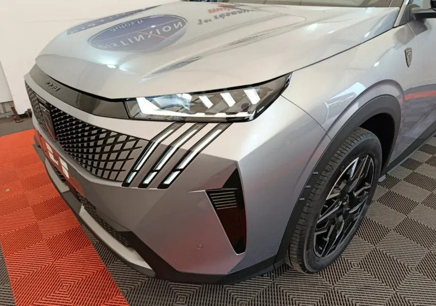 Vue 3/4 avant droit du Peugeot 3008 gris clair avec phares LED et calandre au design géométrique marqué.