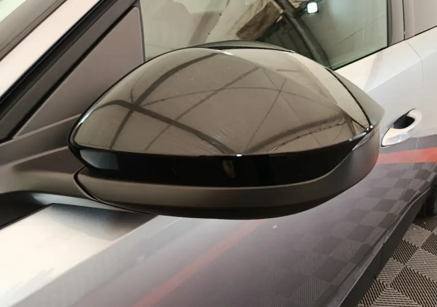 Rétroviseur noir en gros plan côté gauche sur Peugeot 3008 gris clair, avec reflet de la structure du plafond.