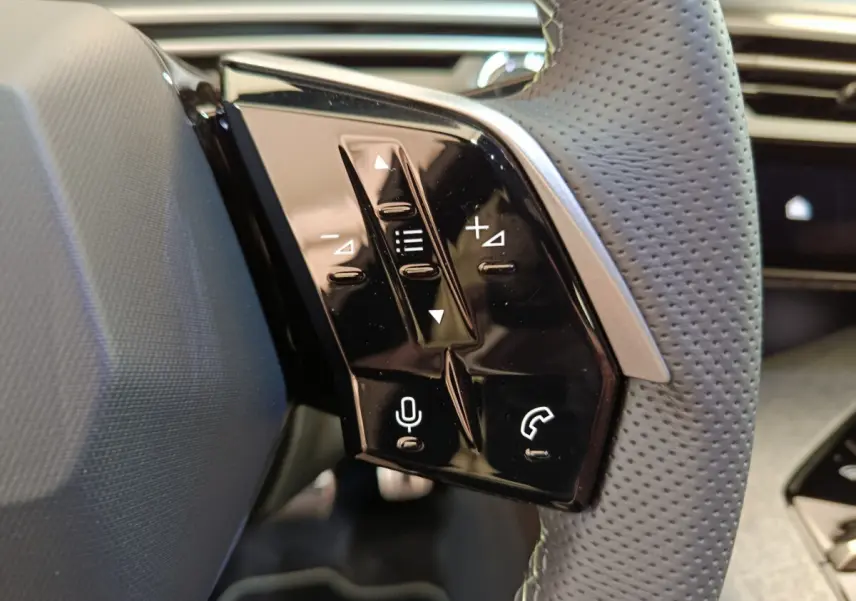 Gros plan sur les commandes tactiles noires du volant cuir perforé du Peugeot 3008 gris clair, version hybride 2025.