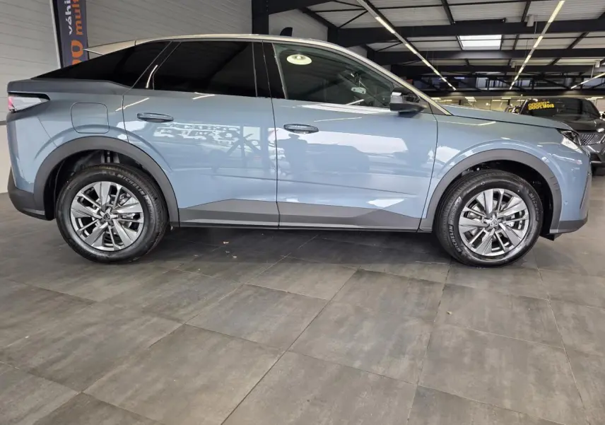 Vue de profil côté gauche d'un Peugeot 3008 hybride bleu métallisé avec jantes alliage 18 pouces en intérieur showroom.