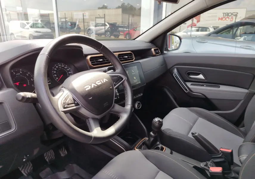 Vue intérieure côté conducteur du Dacia Duster 2024, volant multifonction, boîte manuelle et tableau de bord moderne.