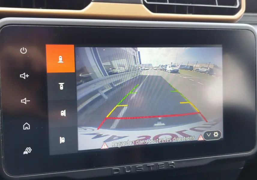 Écran de caméra de recul du Dacia Duster 2024, vue arrière avec lignes de guidage colorées sur route asphaltée.