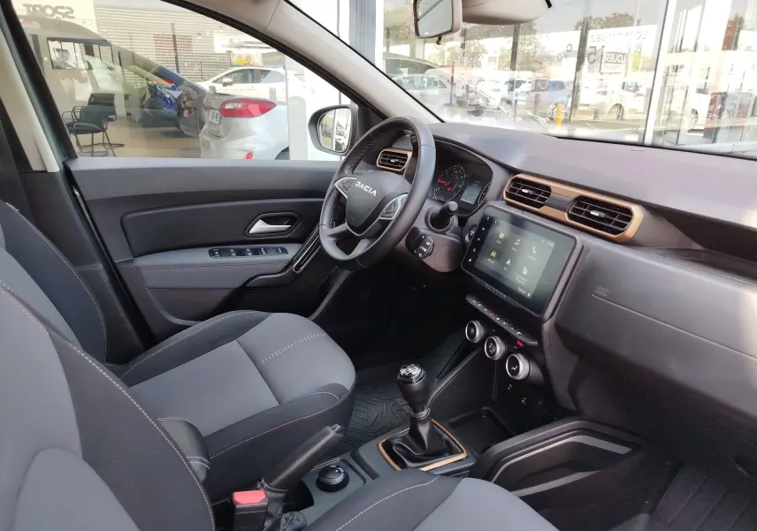 Vue intérieure côté conducteur du Dacia Duster 2024, montrant le volant, la console centrale avec écran tactile et levier de vitesses manuel.
