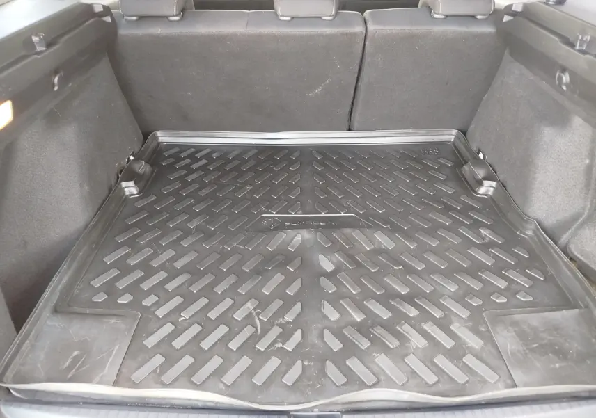 Coffre ouvert vu de l'arrière d'un Dacia Duster 2024, avec tapis de protection noir et sièges arrière rabattus.