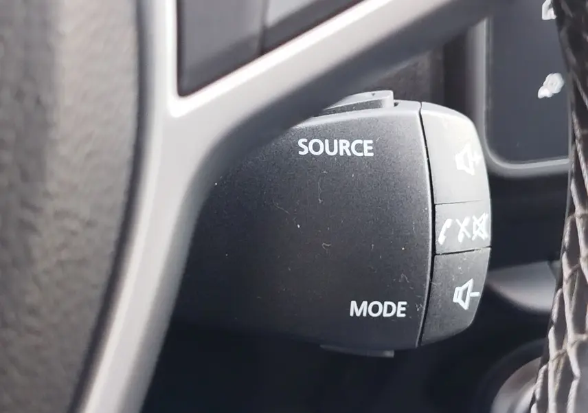 Détail du commodo audio avec boutons source et mode sur le volant d’un Dacia Duster 2024, intérieur noir.
